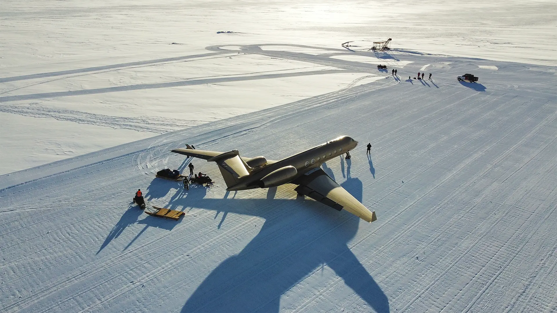 Private jet parked on a snow-covered runway in Antarctica, with snowmobiles and crew preparing for a expedition.