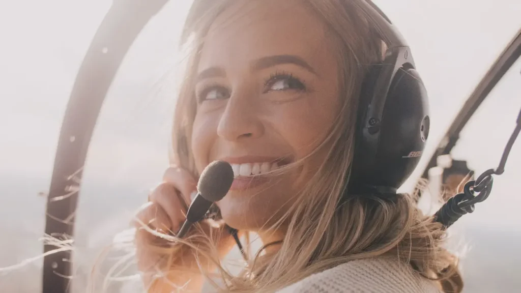 Smiling woman wearing a headset inside a helicopter.