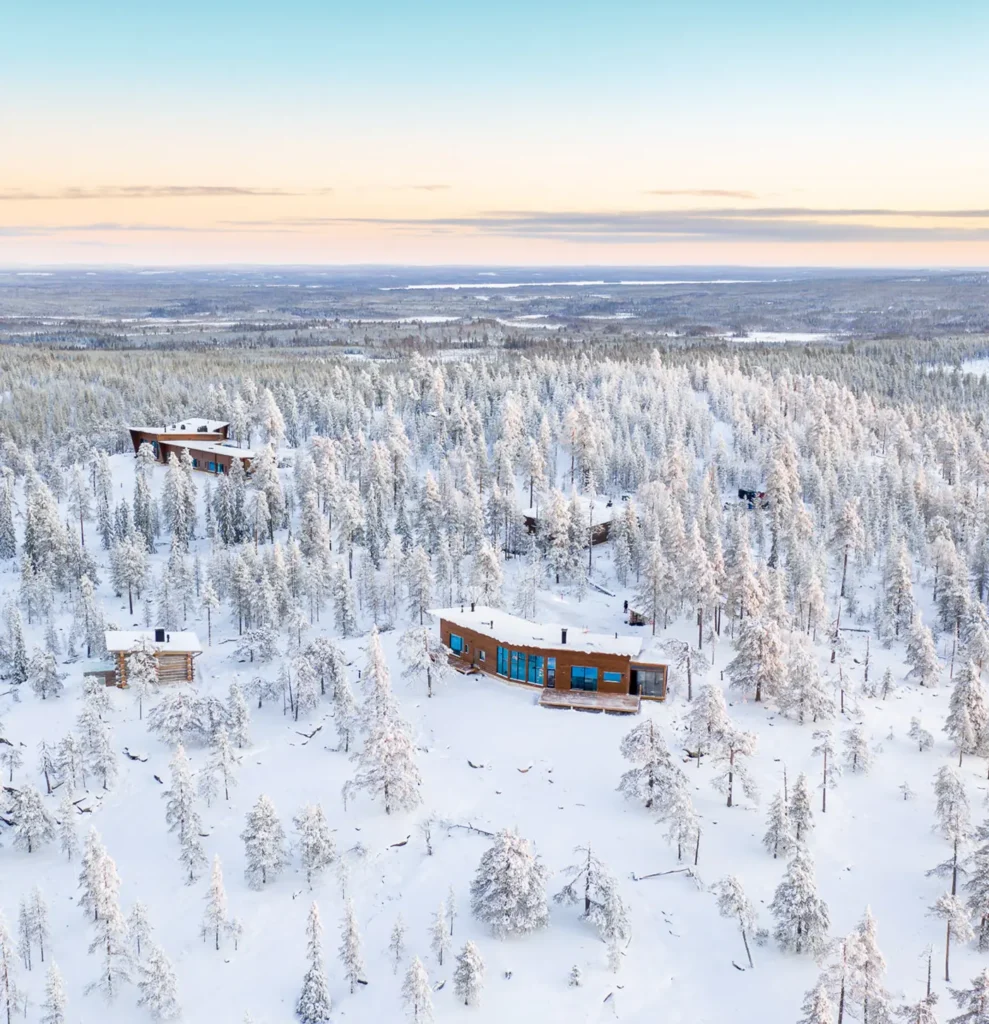 Aerial view of luxury cabins nestled in a snow-covered forest, showcasing a serene winter retreat experience