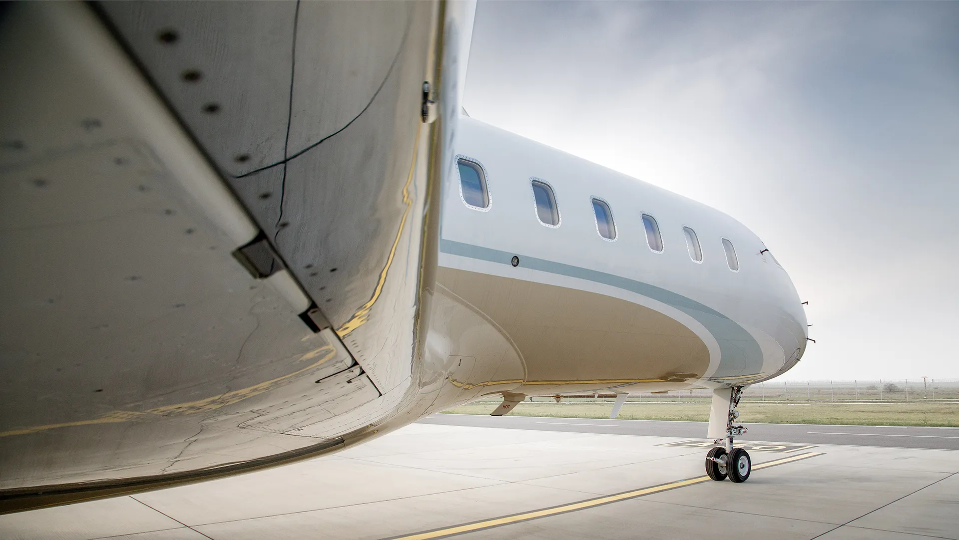 Close-up view of the featured aircraft from Avcon Jet: a Bombardier Global 5000, highlighting its sleek fuselage and windows with a soft sky and airport tarmac in the background.