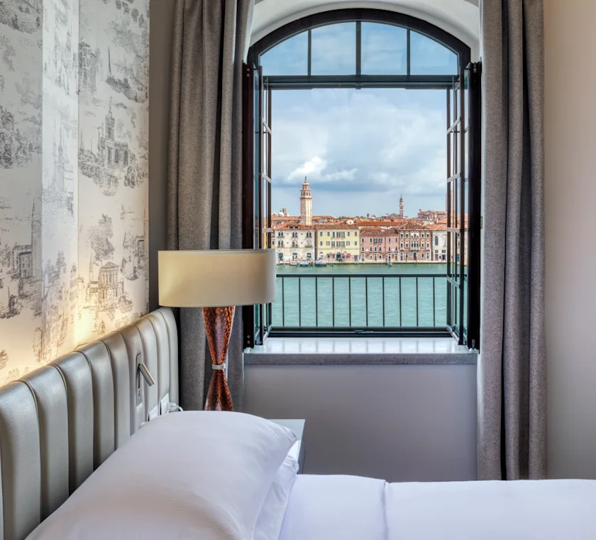 The Hilton Molino Stucky Venice, beautifully lit at dusk, overlooks the calm Venetian canals, creating a perfect romantic setting for Valentine's Day. The historic architecture and waterfront views offer an enchanting escape for couples.